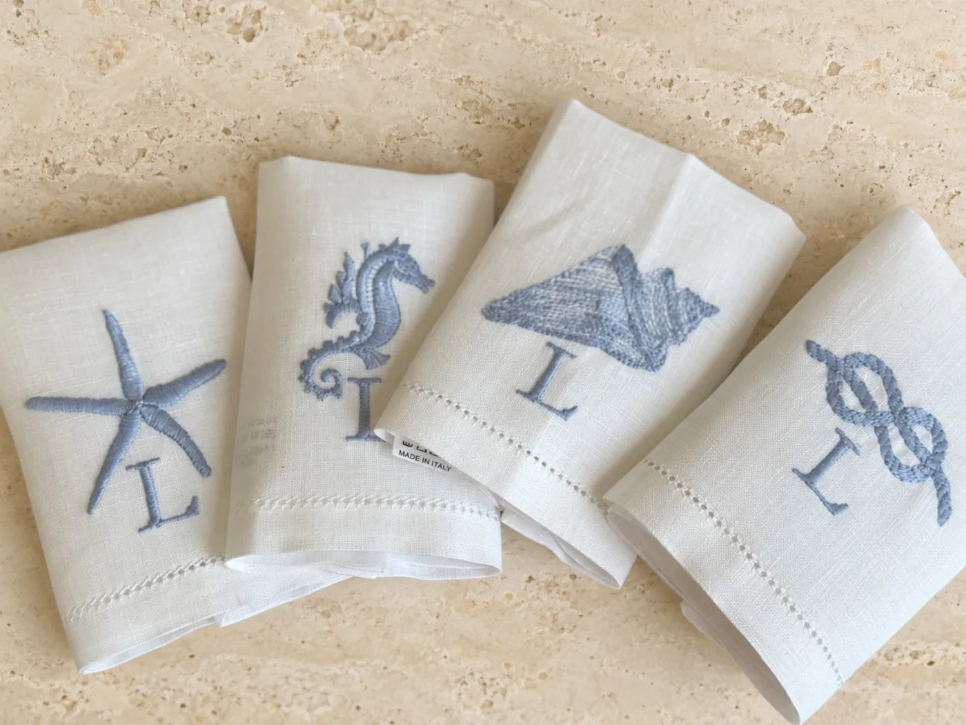 White linen napkins embroidered in blue with a starfish, seahorse, shell and knot