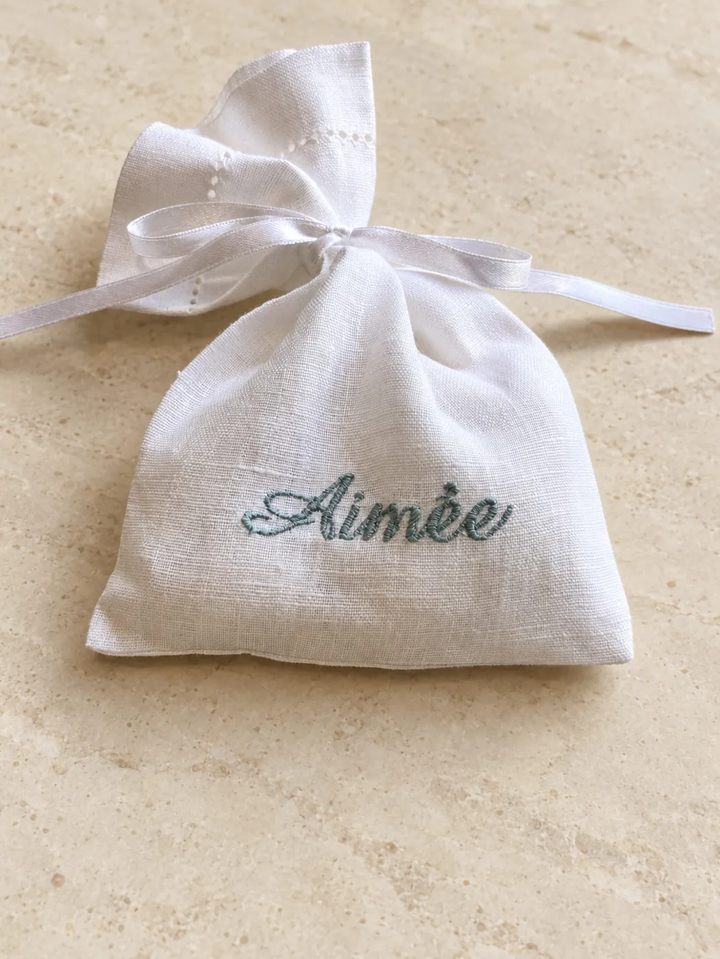 White linen pouch embroidered with a name in soft blue script