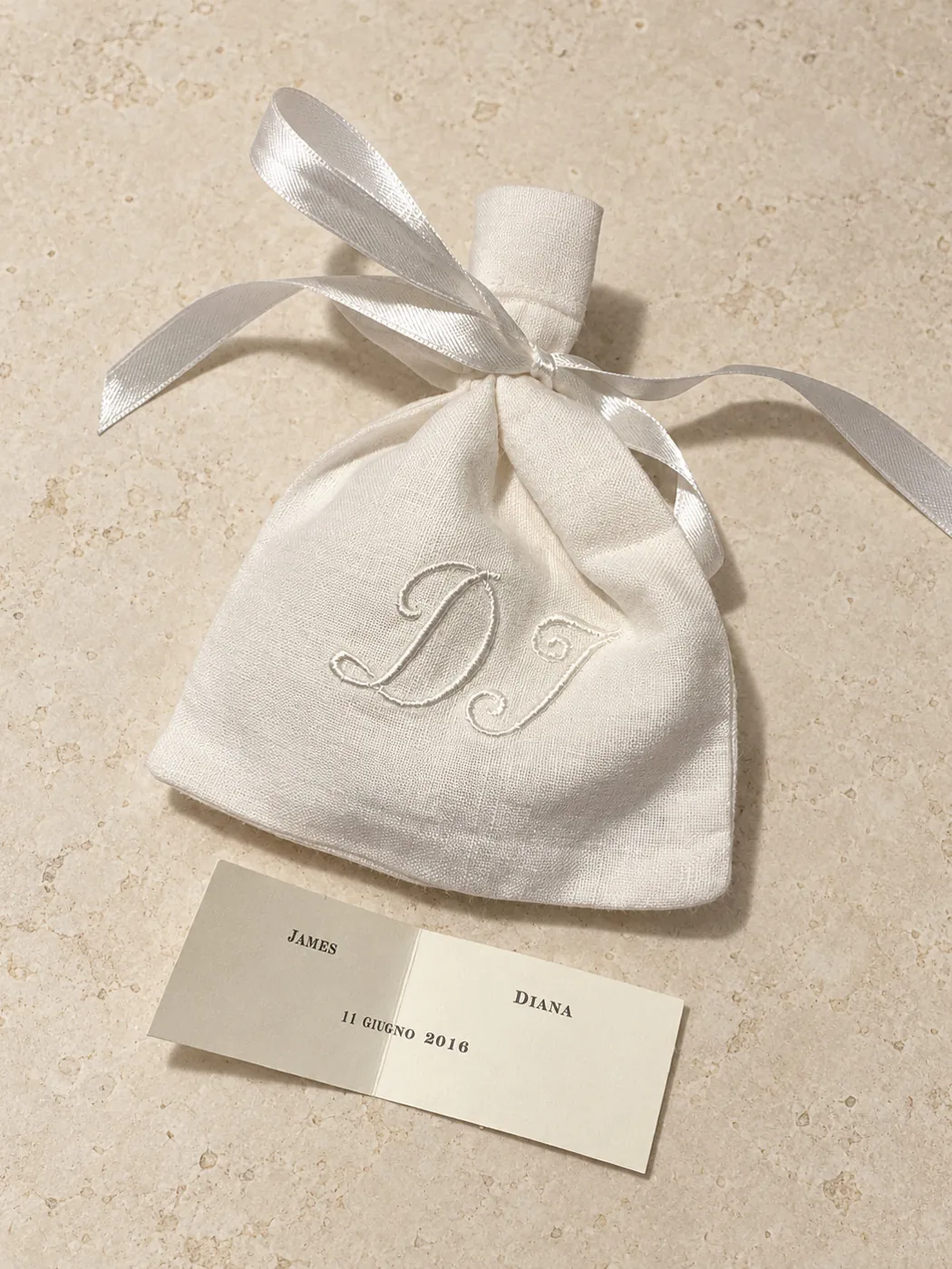 White linen pouch with white embroidered initials and a satin ribbon